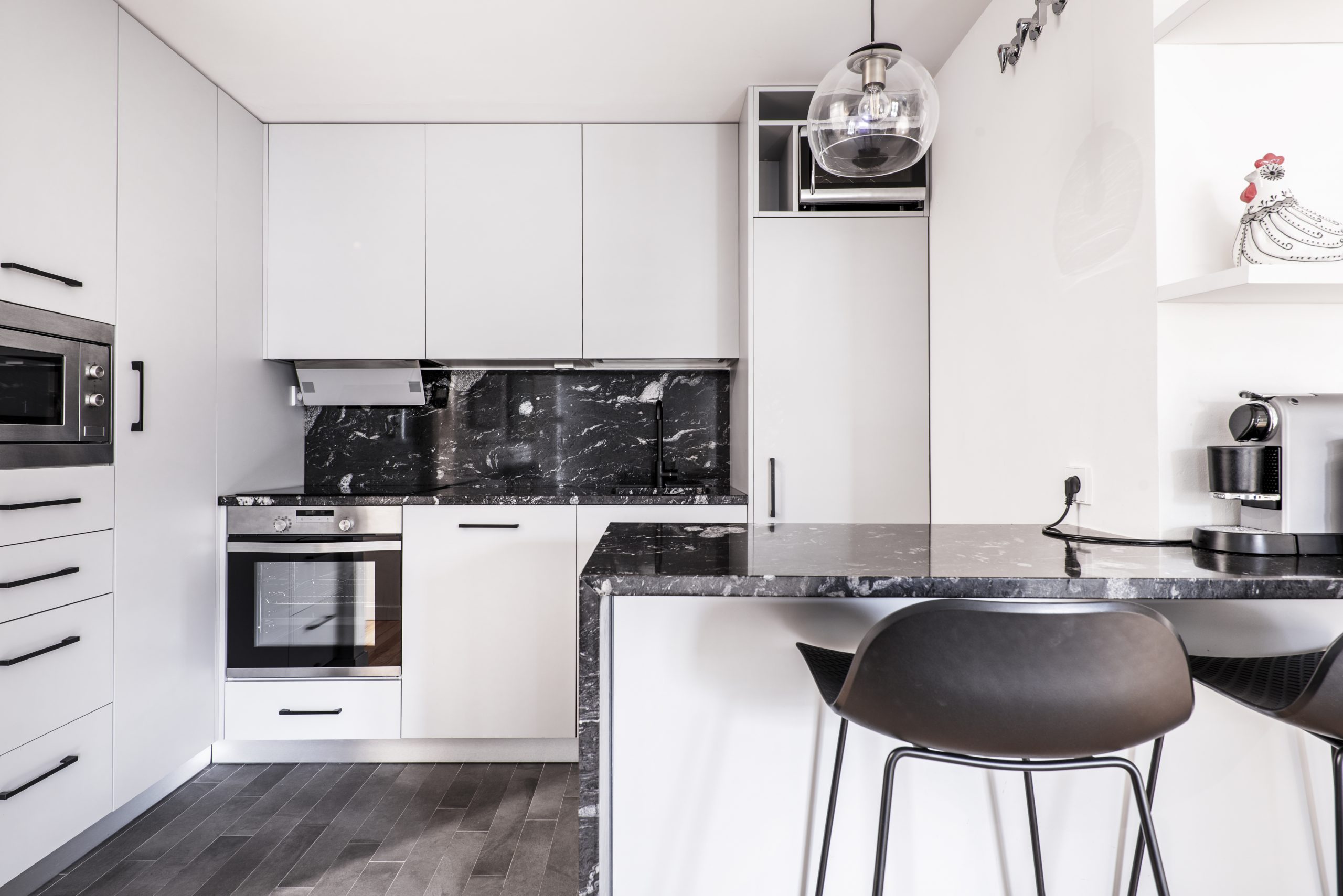 Full kitchen with white floor-to-ceiling furniture, black marble countertops with white veins, gray stoneware floors and tall metal and black resin chairs